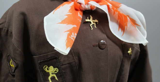 Colour photograph of a vintage Embers uniform. It is brown with a white and orange scarf