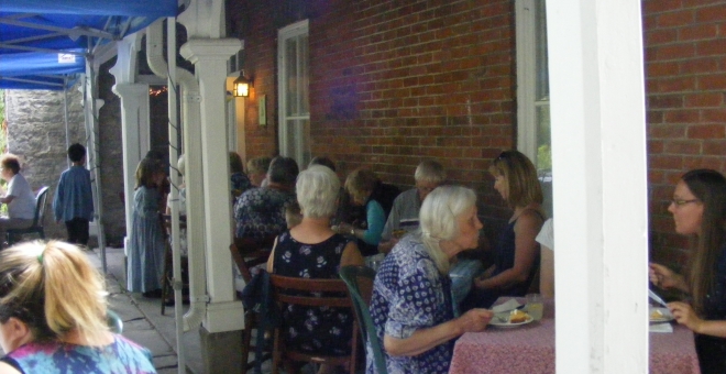 A group of people seated at tables in front of a brick wall. There are white columns between tables. 