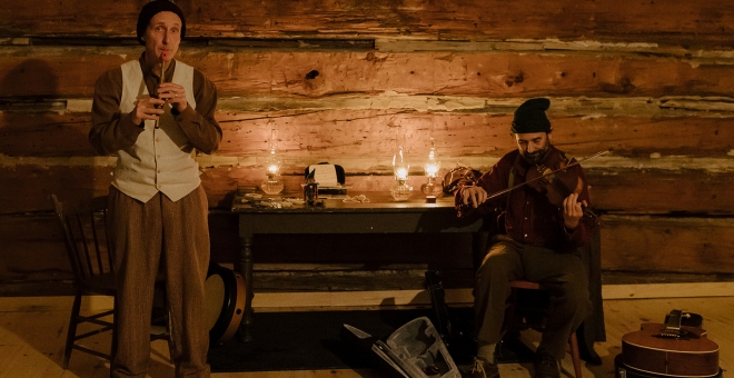 Two men playing a fiddle and a whistle by lantern light